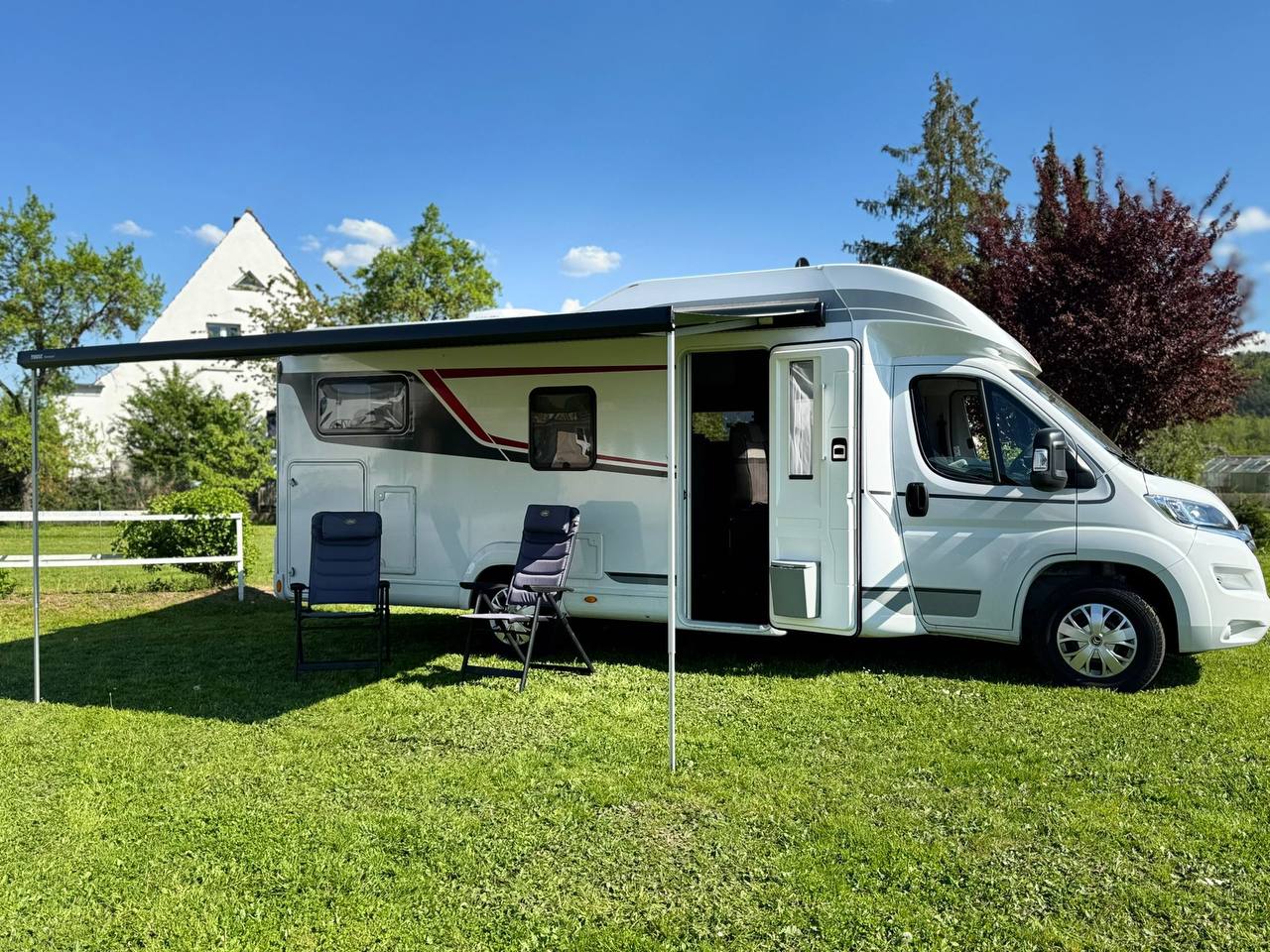 Wohnmobil mit ausgefahrener Markise und Campingstühlen auf der Wiese